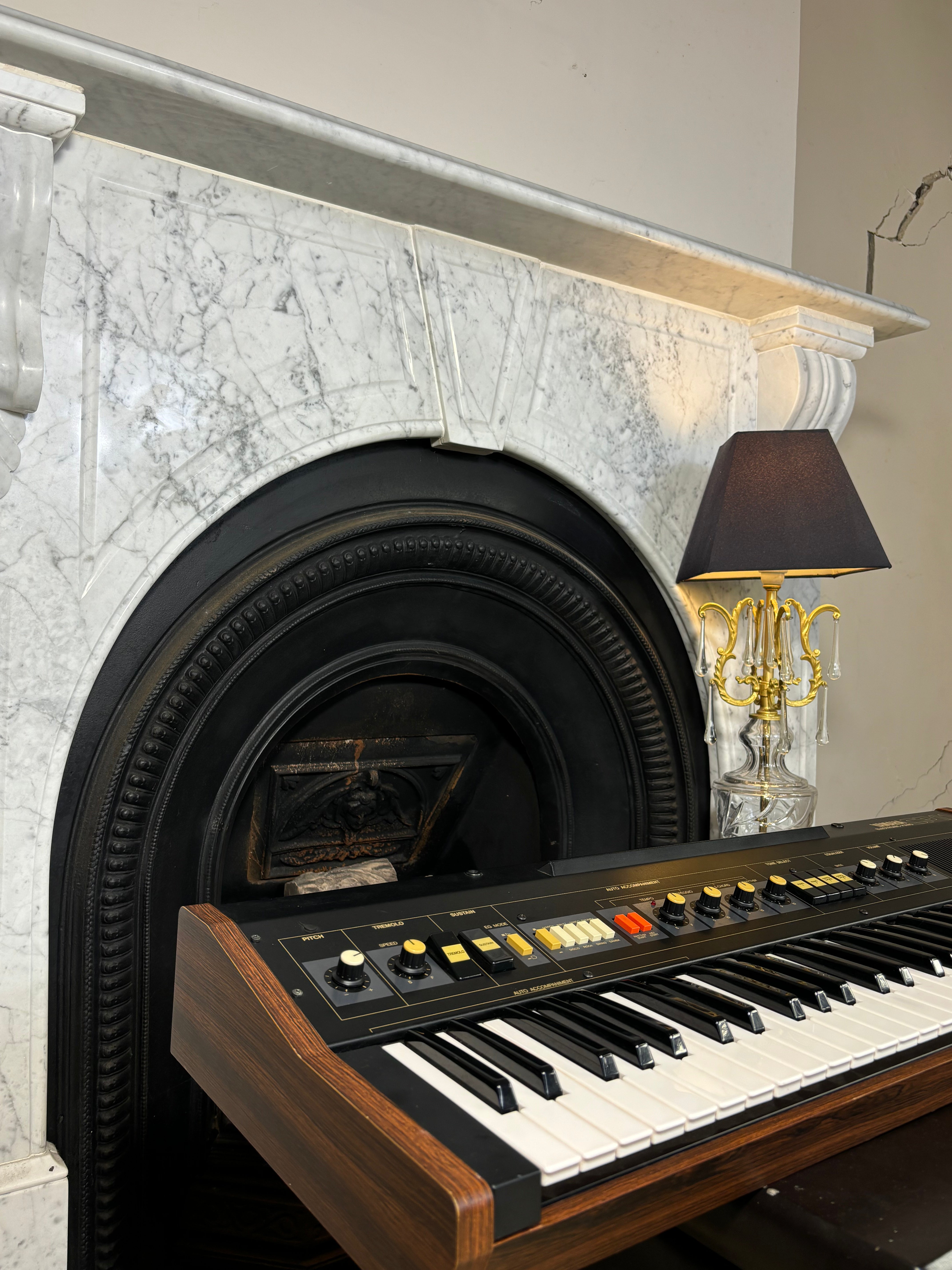 Piano in front of a marble fireplace with a lamp on a side table.