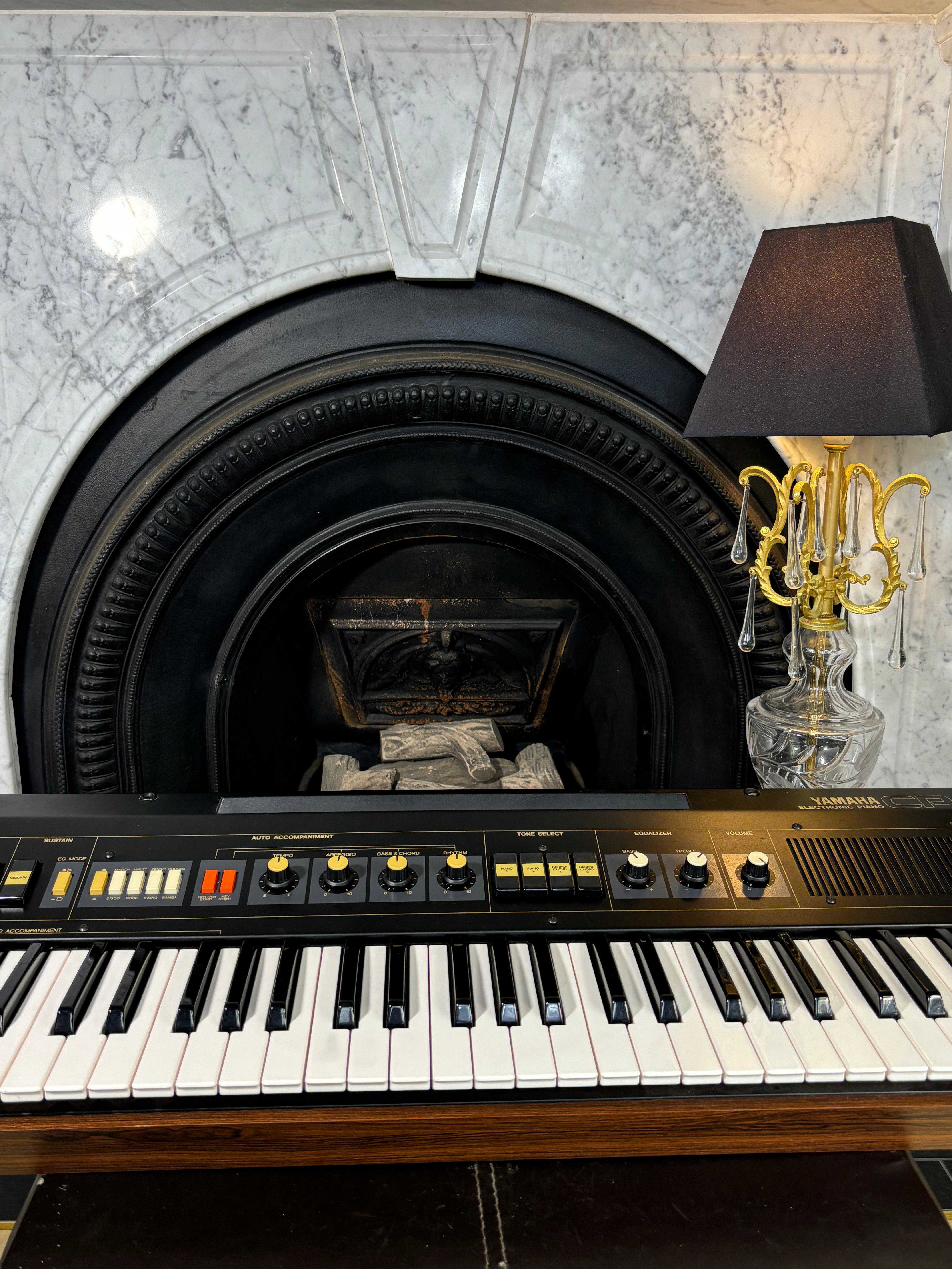 Yamaha_CP-11  in front of a fireplace with a lamp on a marble ledge.